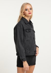 Giacca in denim nera con un taglio classico, dotata di bottoni frontali, tasche laterali e una texture leggermente sbiadita. Accentuata da un collo a revers.