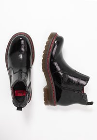 Ett par blanka svarta ankelskor med röd sömnad, bruna robusta sula, sidodragkedja och grå innerfoder på en vit bakgrund.