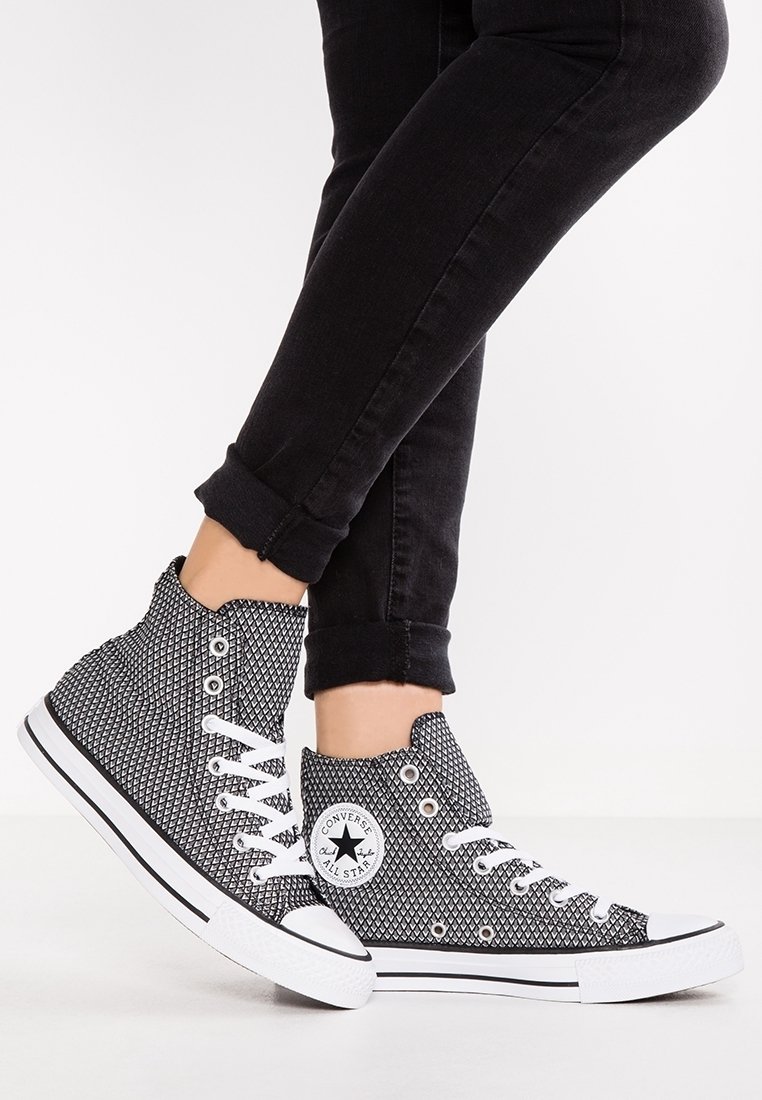 Sneaker alte in bianco e nero con un motivo testurizzato, lacci bianchi e suole in gomma, caratterizzate da un logo circolare sul lato.