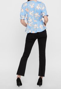 Blusa peplum floreale blu con maniche corte, abbinata a jeans neri a zampa d'elefante e tacchi neri; tessuto morbido e sottili righe orizzontali.