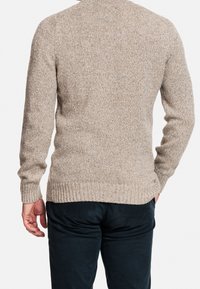 Béžový pletený svetr s žebrovanými manžetami a lemem, s texturovanou směsí vláken. Nošený přes tmavé kalhoty, zobrazen zezadu a s přiléhavým střihem.
