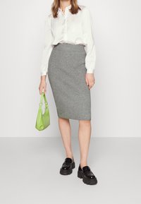 Grå randig blyertskjol i kombination med en vit satinknappad blus. Håller en liten grön handväska. Svarta kraftiga loafers fulländar looken.