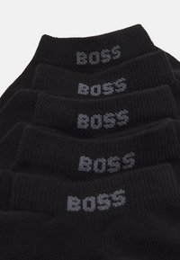Sorte sokker med ribbet tekstur, der viser en grå "BOSS"-logo på skaftet. Fem sokker stablet med toppen justeret for synlighed.