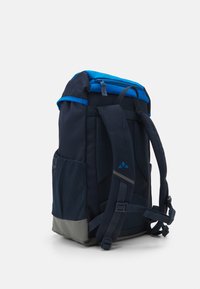 Mochila azul marino con una base gris, correas acolchadas, bolsillos laterales de malla y una parte superior con cremallera, que presenta un borde y acentos de diseño en azul contrastante.