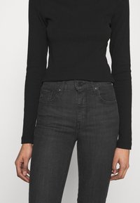 Top de manga larga negro con textura acanalada combinado con vaqueros de tiro alto gris oscuro que presentan bolsillos frontales y detalles de costura sutiles.