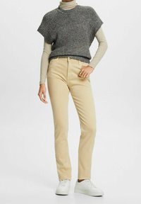 Jeans beige ajustados de cintura alta, combinados con un suéter corto y suelto de punto oscuro. Zapatillas blancas completan el atuendo.