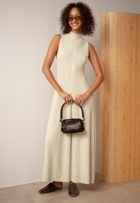 Megztinis, be rankovių, kreminės spalvos su aukštu apykakle ir vertikaliu briaunavimu, derinamas su juoda rankine ir leopardo rašto mulo.