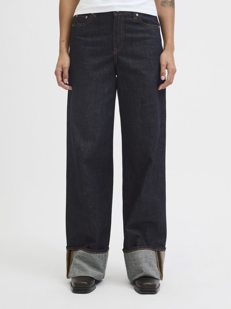 Jeans de ganga escura de perna larga com costura laranja, apresentando barras dobradas de tecido cinza claro e bolsos frontais.