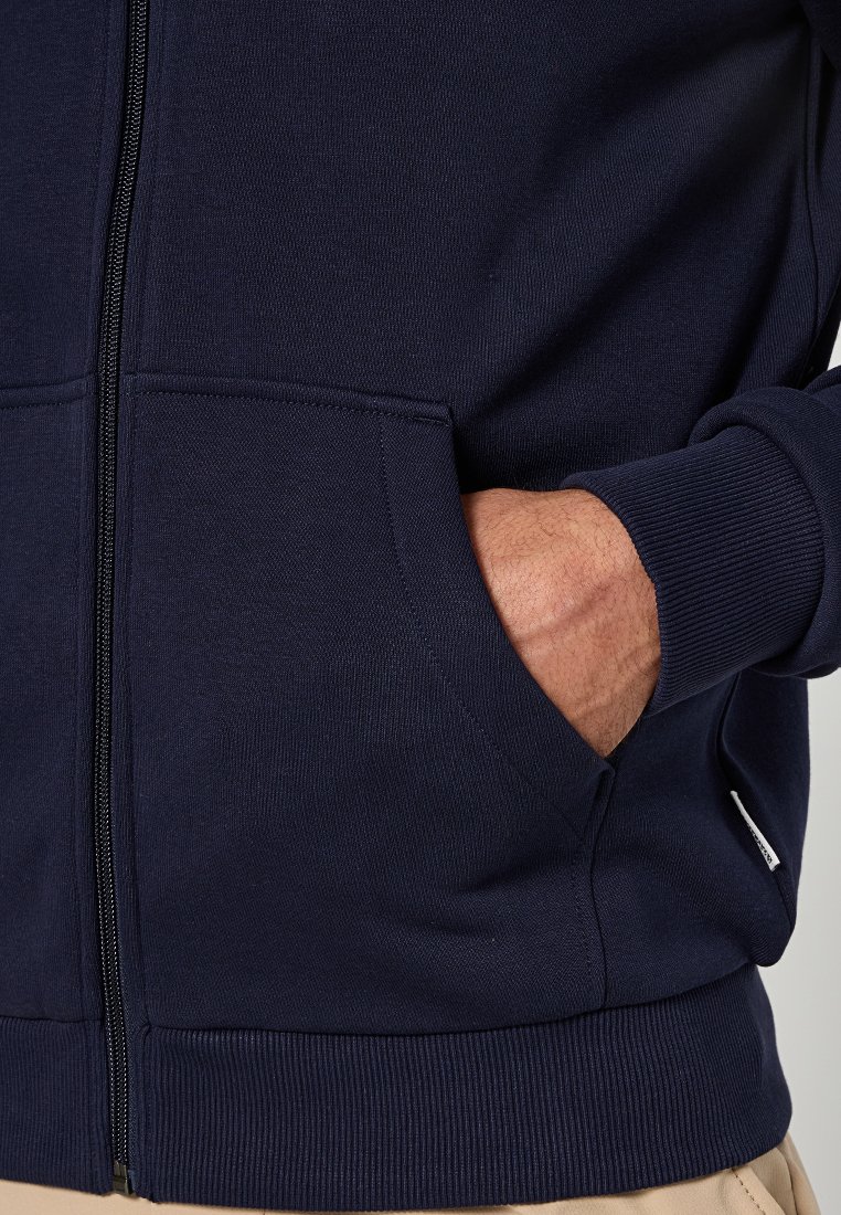 Marineblaue Zip-Hoodie mit gerippten Bündchen und Saum, ausgestattet mit einer Fronttasche und strukturierten Stoffdetails.