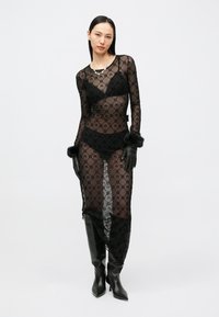 Διάφανο μαύρο φόρεμα με φλοράλ δαντέλα, μακριά μανίκια και σκίσιμο μέχρι το μηρό· συνδυασμένο με μαύρα γάντια και μπότες με τακούνι μέχρι το γόνατο.