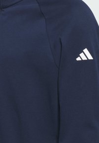 Sweatshirt bleu marine en tissu texturé, arborant un logo à trois rayures blanches sur l'épaule. Design sportif classique avec une silhouette ajustée.