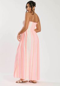 Platslös maxiklänning i krämvit med rosa vertikala ränder och geometriska mönster. Har ett smockat bodice och flödar ned till golvet.