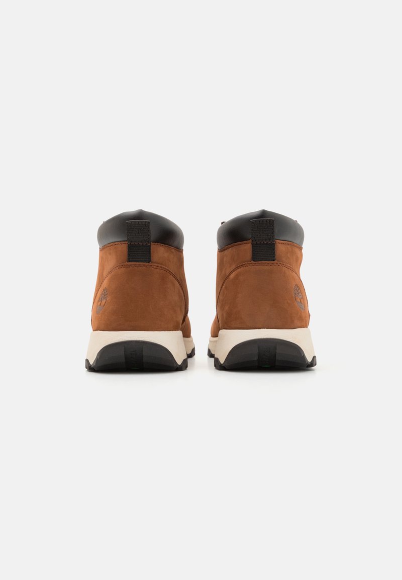 Bottines en daim marron avec des accents en cuir noir, un col rembourré et une semelle intermédiaire blanche. Présente un logo sur le talon extérieur.