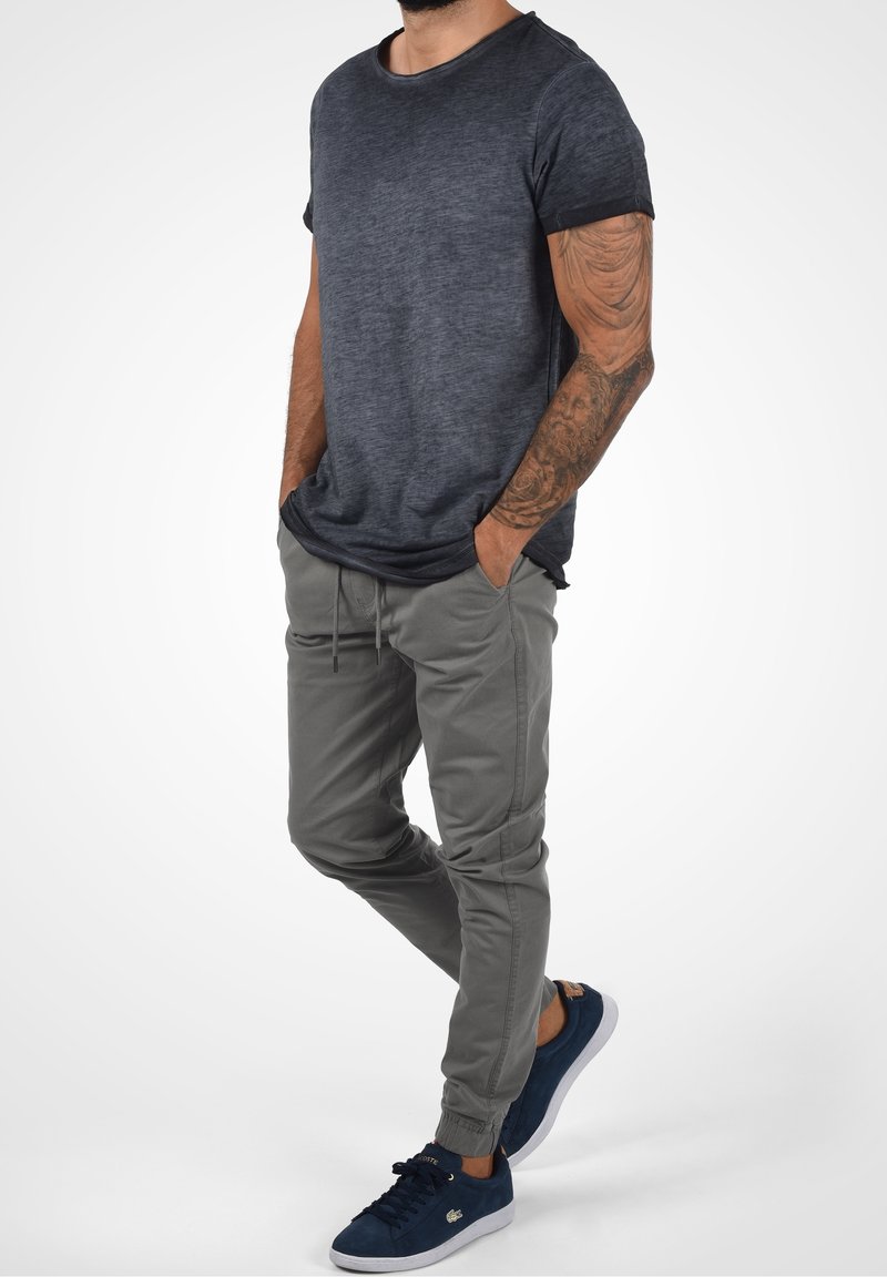 Camiseta de color gris oscuro texturizada con mangas cortas, combinada con pantalones jogger de color gris claro con puños elásticos y bolsillos laterales. Llevado con zapatillas de deporte de color azul marino.