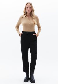 Beige ribbel lange mouwen top met knoopsluiting en kraag, gecombineerd met zwarte tapered broek en zwarte enkellaarsjes.