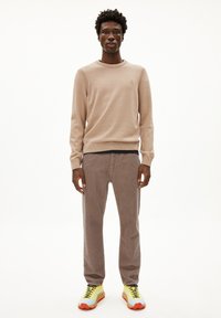 Helle beigen Strickpullover mit Rippbündchen, kombiniert mit braunen Cordhosen und klobigen gelben Sneakers mit blauen und orangenen Akzenten.