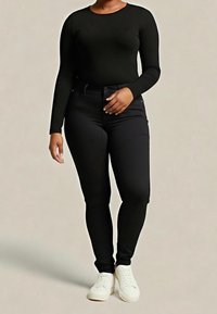 Haut noir à manches longues et ajusté, associé à un jean skinny noir, porté avec des baskets blanches. Texture lisse, design simple, sans motifs visibles.