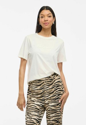 T-shirt en coton blanc à manches courtes avec un design texturé "équilibre", associé à un pantalon rayé beige et noir.