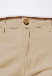 Beiga bomullsshorts med en synlig knapp och dragkedja, med sydda detaljer och en slät yta.