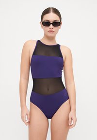 Bikini violet avec un design à col haut, présentant un panneau en maille au niveau de la taille. Texture lisse, bas taille haute, branding minimal.