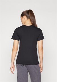 Svart t-skjorte med korte ermer laget av bomull, med rund hals og en tettsittende design med glatt tekstur. Visning av baksiden.