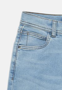 Κοντινή λήψη ανοιχτό μπλε τζιν με λεπτομέρειες στην μπροστινή τσέπη, στην τσέπη για κέρματα και στις ραφές της θηλιάς για ζώνη σε λευκό φόντο.