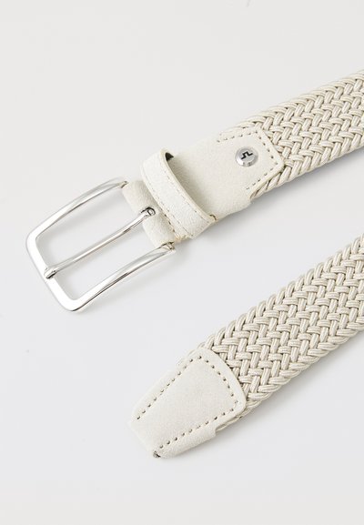 Geweven beige riem van elastisch materiaal met een gestructureerd oppervlak en een zilveren metalen gesp. Heeft een faux suède punt en accenten.