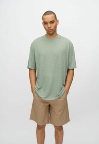 Camiseta de corte holgado y manga corta en tela verde claro, combinada con pantalones cortos beige. La camiseta tiene un cuello redondo y una textura suave.