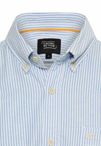 Lyseblåstribet skjorte med knapper, bomuldsstof, spidst krave, fire knapper, lille lommedetalje med logo, indendørs belysning.