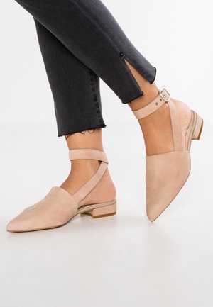 Ballerines slingback beige à bout pointu avec brides à la cheville, portées avec un jean noir court avec fentes latérales.