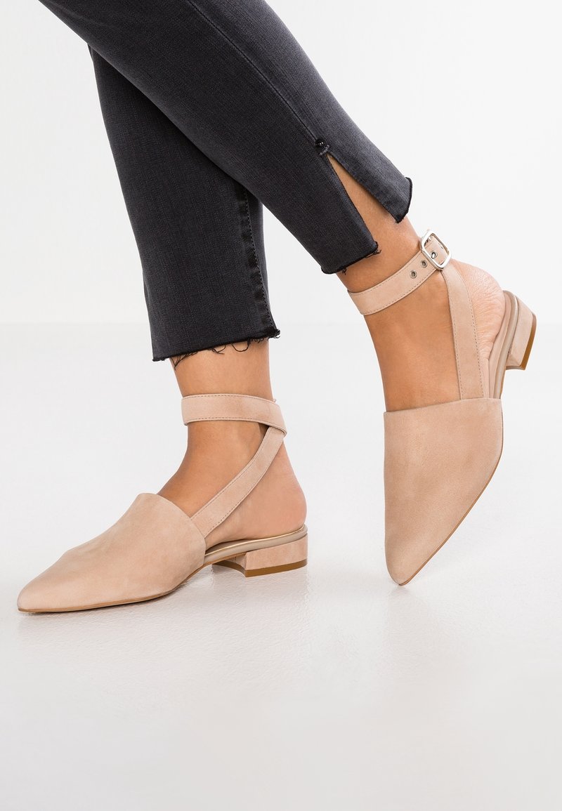 Ballerines slingback beige à bout pointu avec brides à la cheville, portées avec un jean noir court avec fentes latérales.