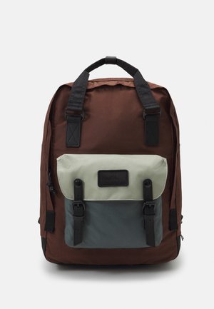Sac à dos en tissu brun avec un rabat avant vert et gris, comportant des accents noirs, deux bretelles réglables et deux boucles en plastique.