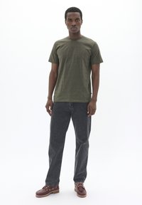 Tricou din bumbac de culoare verde măsliniu cu guler rotund, asortat cu blugi din denim gri închis și pantofi din piele maro cu șireturi și găici.