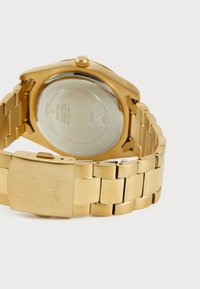 Montre-bracelet en métal doré avec une finition polie, dotée d'un bracelet à maillons, d'une couronne courte et d'un fond de boîte lisse et réfléchissant.