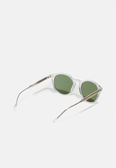 Ochelari de soare cu rame clare și lentile verzi, de formă rotundă, cu brațe subțiri din metal accentuate cu aur. Au un design elegant și minimalist.