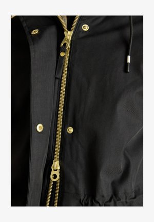 Sort stofjakke med guld detaljer, frontlynlås og trykknapper. Struktureret stof med en glat overflade.