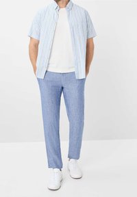 Camicetta a righe blu chiaro e bianco a maniche corte, t-shirt bianca sotto, abbinata a pantaloni in lino blu chiaro e sneaker bianche.
