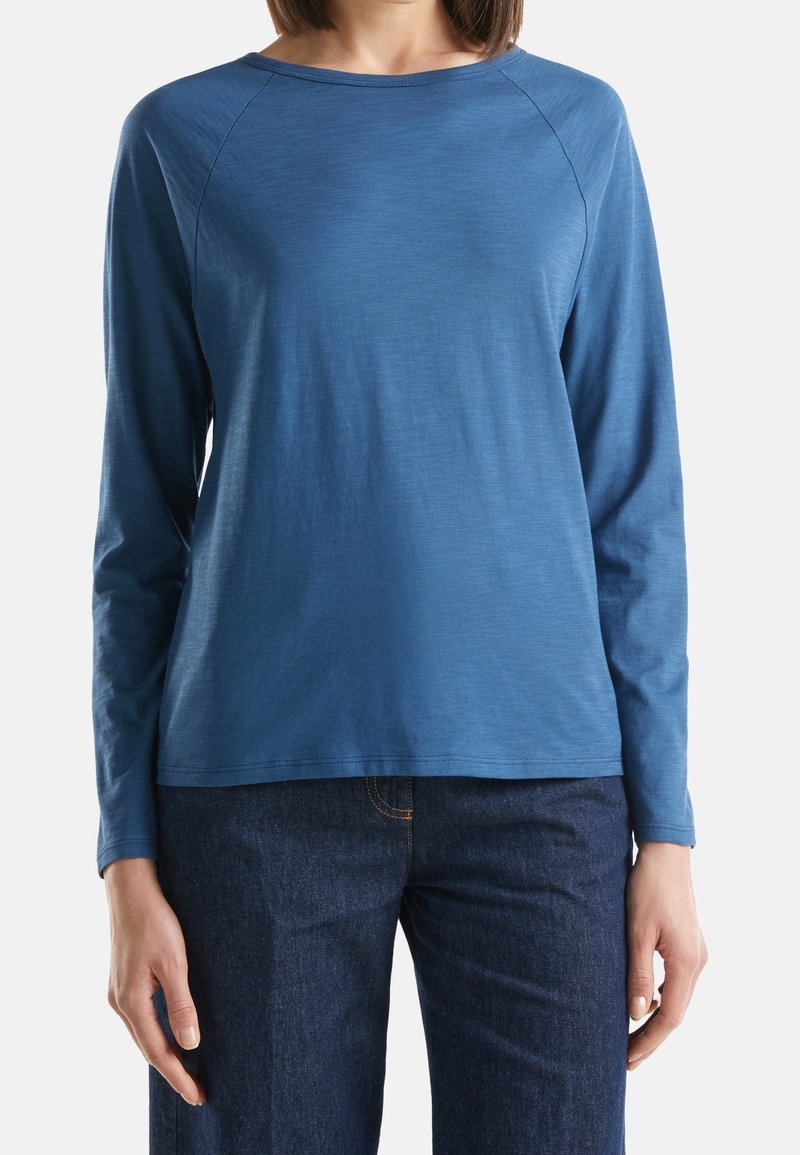 Långärmad, rundhalsad skjorta av mjukt blått tyg; har raglanärmar och en avslappnad passform, matchad med mörka jeans.