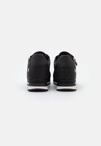 Chaussures de sport noires à tige lisse, accents blancs et design profilé. Dotées d'une fermeture éclair latérale.