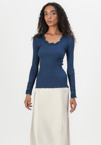 Top de manga longa canelado em azul-marinho com decote em forma de escalope e detalhes em renda nas mangas, combinado com uma saia de seda creme.