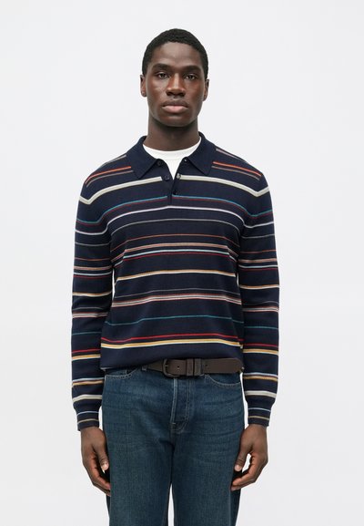Marineblauw gestreept poloshirt met lange mouwen met meerkleurige horizontale lijnen, een kraag en knoopsluiting, gecombineerd met een blauwe spijkerbroek en een bruine riem.