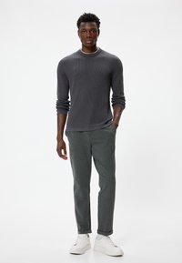 Maglietta a maniche lunghe grigia a coste, taglio rilassato, abbinata a pantaloni grigi a sigaretta. Il modello indossa sneaker bianche. Semplice, senza motivi o dettagli visibili.