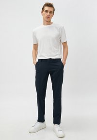 Biała koszulka z krótkim rękawem w zestawieniu z granatowymi spodniami o slim fit. Model nosi białe sneakersy, prezentując casualowy strój.