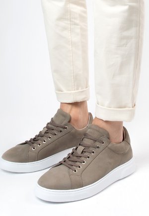 Grijze suède sneakers met witte rubberen zolen, voorzien van ronde veters en metalen veterogen, gecombineerd met opgerolde crèmekleurige broeken.