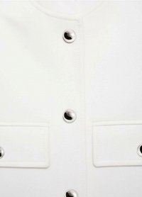 Bijela odjeća s metalnim preklopnim dugmadi, dvije chest džepa s preklopima i glatkom teksturom tkanine. Minimalistički dizajn s fokusom na dugmad.