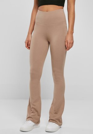 Hellbraune Leggings aus weichem, dehnbarem Stoff mit hohem Bund und ausgestelltem Design, kombiniert mit weißen Sneakers.