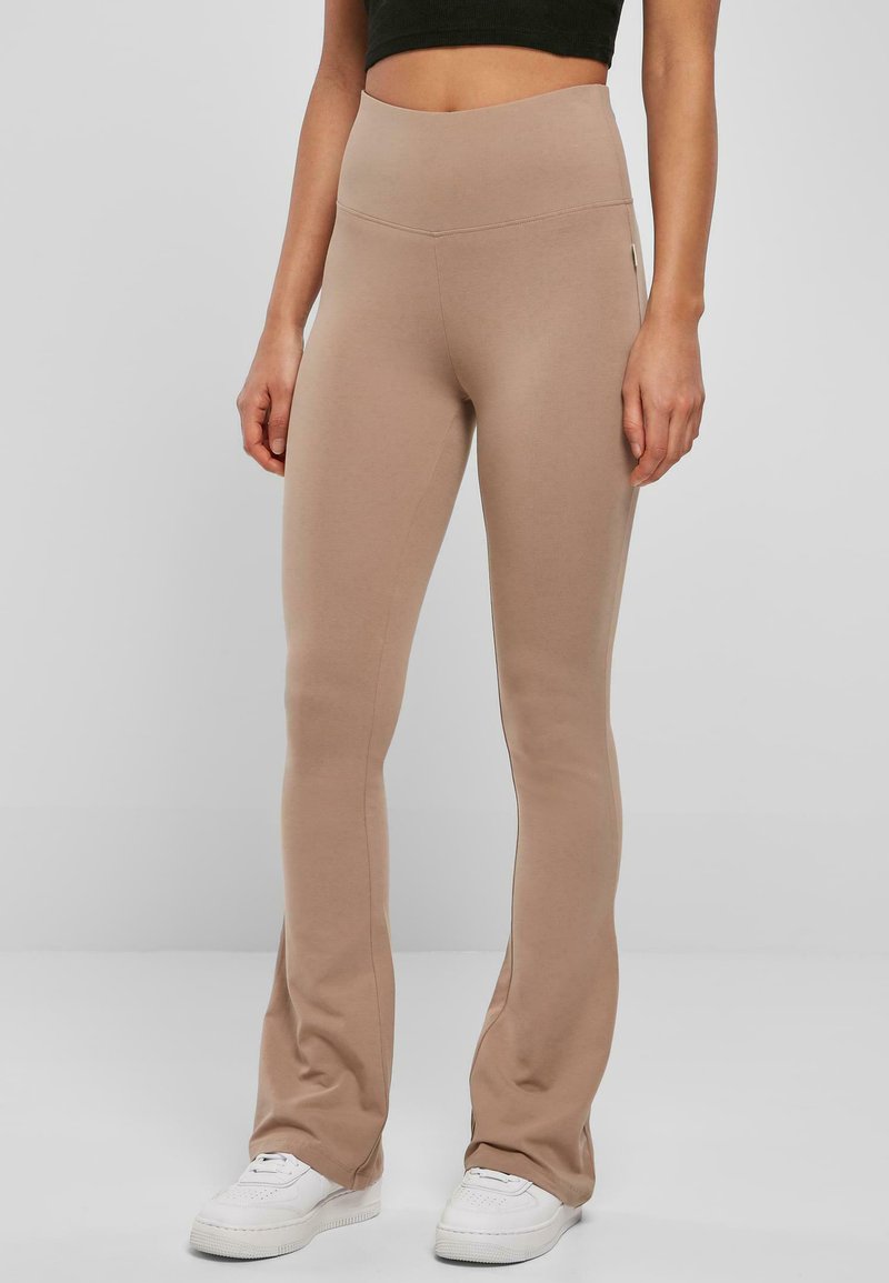 Ljust bruna leggings gjorda av mjukt, stretchigt material med hög midja och utsvängd design, som kombineras med vita sneakers.