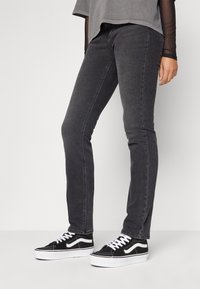 Jeans ajustados grises con una textura suave y un sutil desvanecimiento, combinados con zapatillas de lona en blanco y negro que tienen rayas laterales y cordones.
