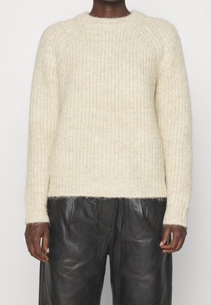 Off-white textured knit sweater paired with loose black leather pants on a person against a plain background.