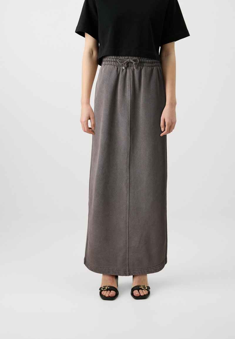 Grauer, langer Rock aus weichem Material mit elastischem Bund und Kordelzug. Kombiniert mit einem schwarzen, kurzen Oberteil und schwarzen Sandalen mit goldenen Akzenten.